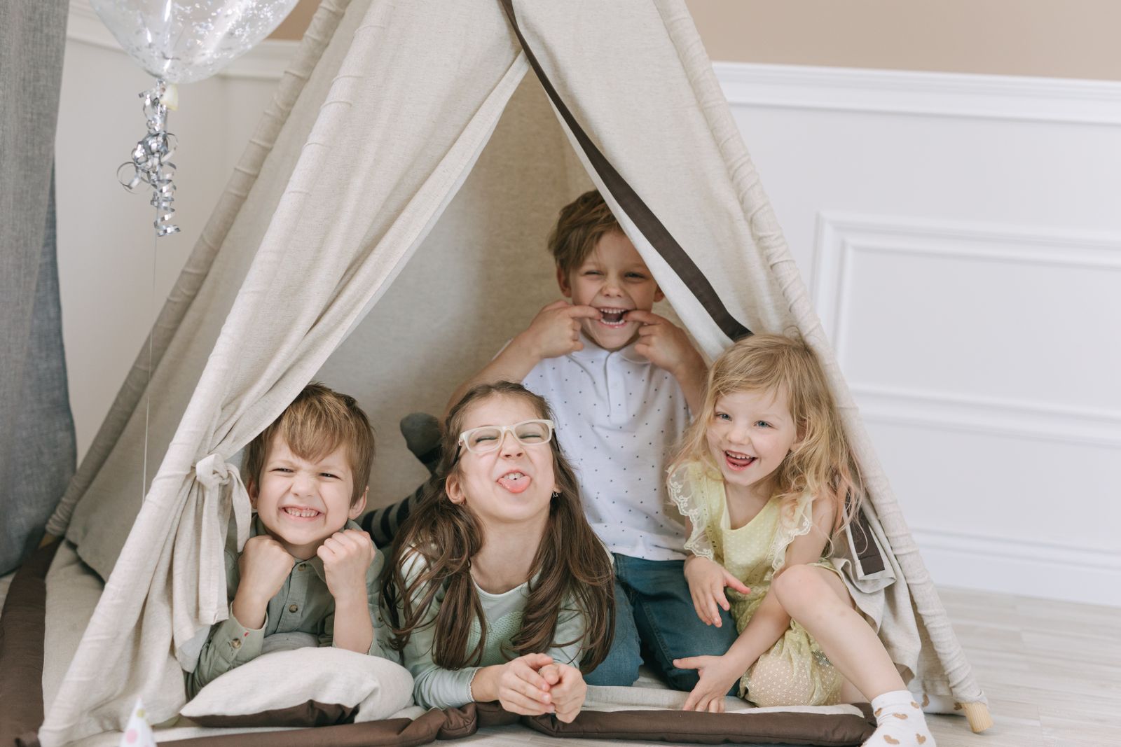 Children sitting inside a blanket fort lit by fairy lights at night