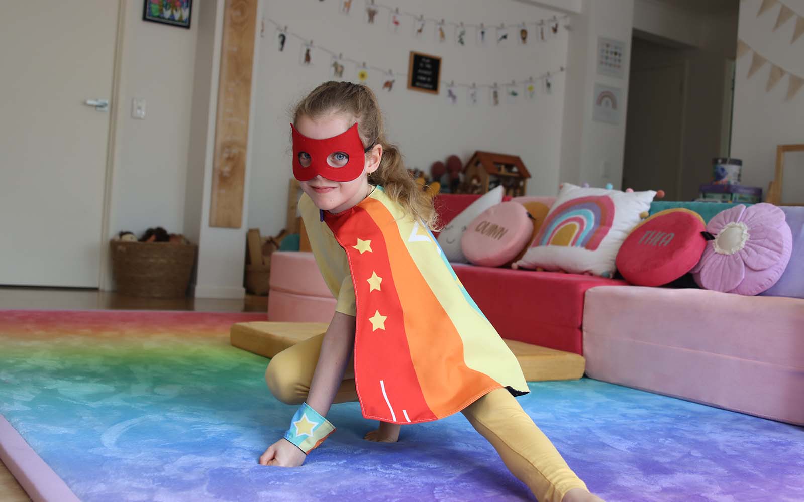 A child wearing the Rainbow Hero Cape Set with arms outstretched
